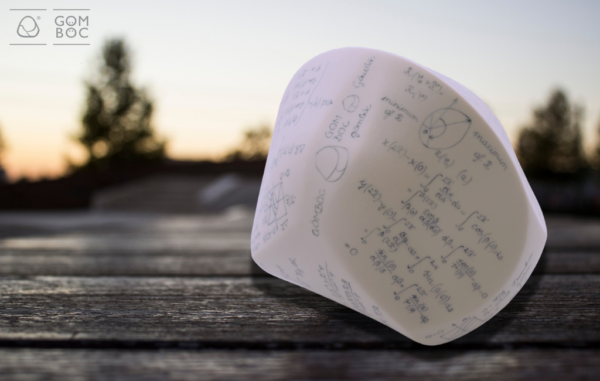 A képen egy Herendi Gömböc látható szabadtéren, fa felületre állítva. A háttérben homályosan fák és naplemente látható.